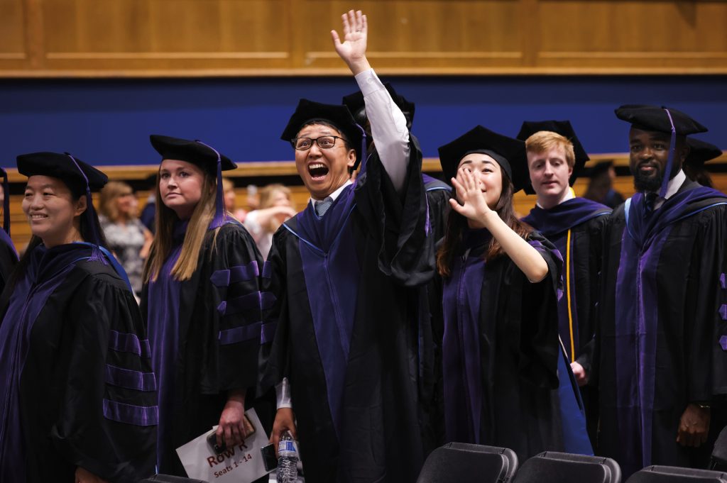 Man in graduation regalia waving