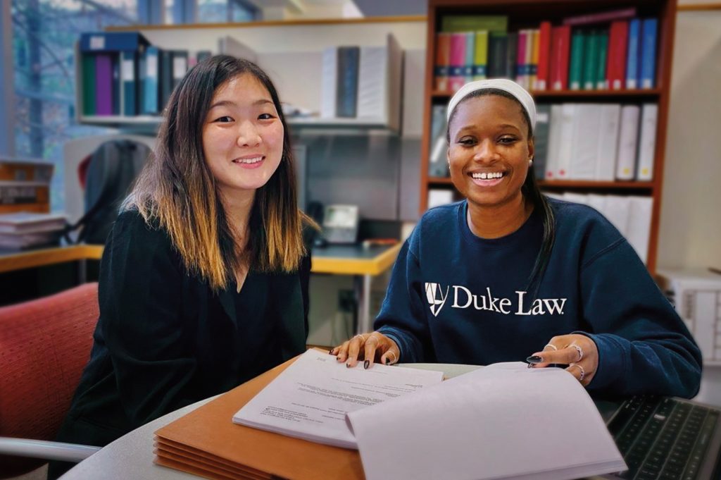 Two women at a table with papers, one wearing a Duke Law shirt